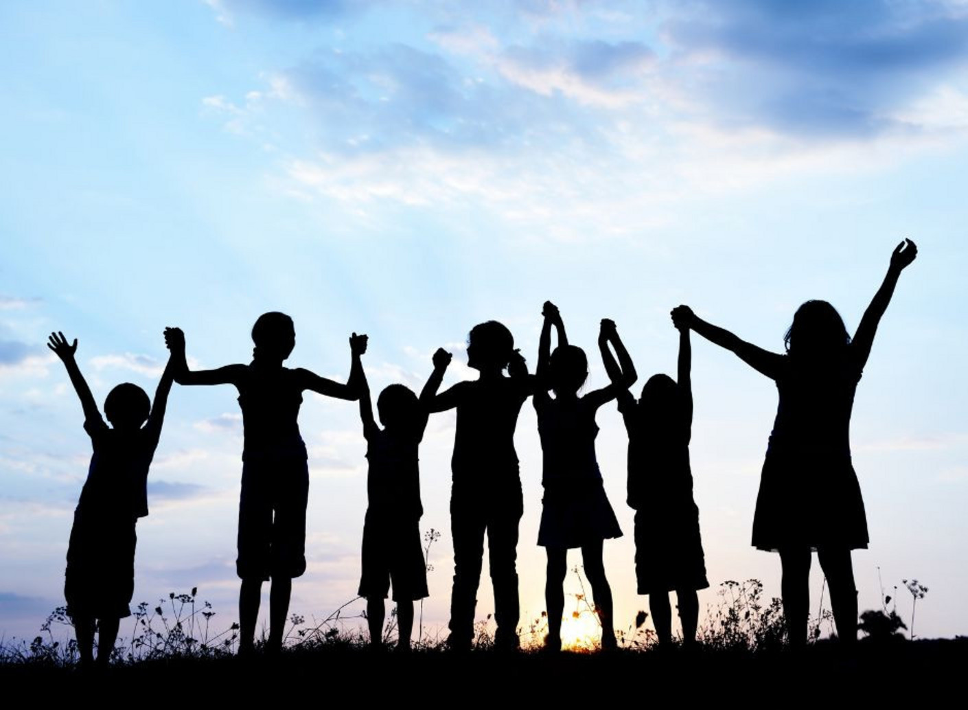 Silhouettes de jeunes enfants, debout en ligne, levant les bras vers le ciel au coucher du soleil. Cette image illustre l’espoir, l’unité et l’inclusion des jeunes en difficulté, dans le cadre de la Journée internationale des droits de l’enfant.
