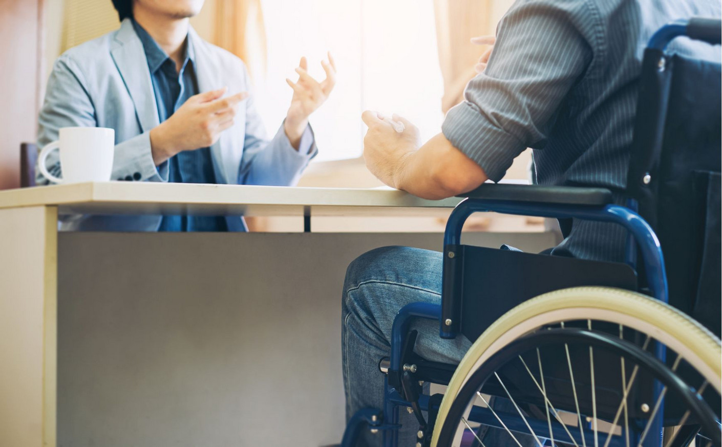 L’inclusion professionnelle par l'apprentissage Une personne en fauteuil roulant discute avec un professionnel assis à un bureau, illustrant l’inclusion et l’apprentissage des personnes en situation de handicap en milieu professionnel.