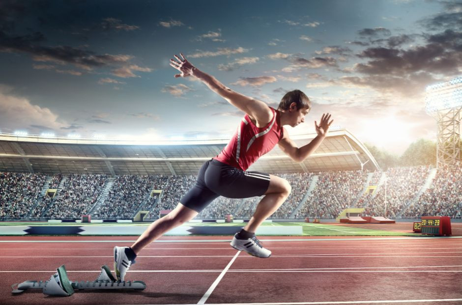 Un athlète en tenue de compétition, en pleine course de sprint sur une piste de stade rempli de spectateurs. L’image capture l’instant où il décolle des starting-blocks, symbolisant la détermination, la rapidité et l’effort nécessaires pour réussir à la fois dans le sport de haut niveau et dans une formation en alternance.