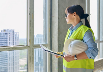 Femme en gilet de sécurité jaune et casque blanc, tenant des plans sur un chantier, illustrant la mixité dans les métiers techniques et l’égalité professionnelle.